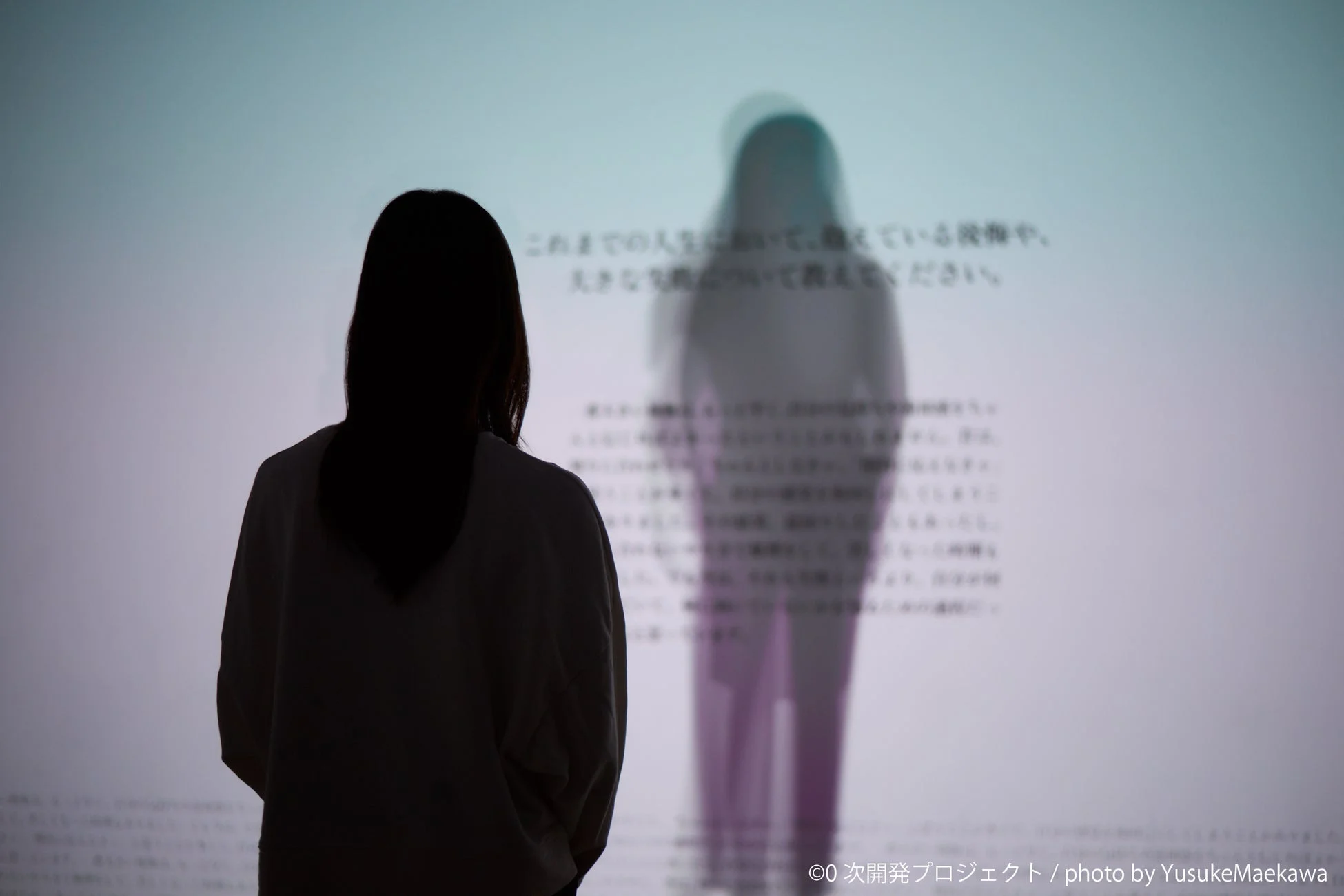 壁に投影されたテキストとぼやけた人影を見つめる人物のシルエット