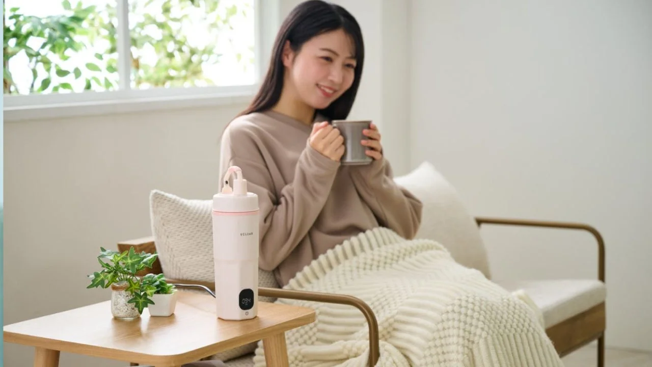 窓辺でリラックスした様子の女性が、マグカップを両手で持ち温かい飲み物を飲んでいます