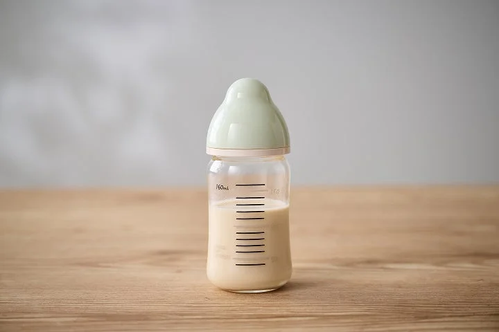 木目のテーブルに置かれたミルク入りの哺乳瓶